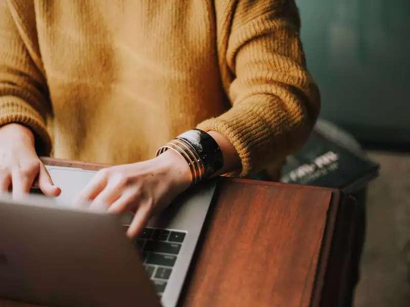 Photo of a person wearing an orange sweater typing at a laptop from the shoulders down